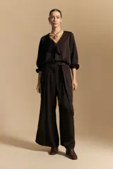 Blusa negra de satén con escote en V y detalle de volados frontales. Presenta mangas largas con puños abotonados y una silueta fluida.