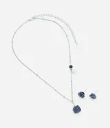 Conjunto de bisutería compuesto por un collar corto y un par de aros tipo botón. El collar presenta una cadena metálica con dijes de piedra natural azul alambrada y una placa circular grabada. Los aros a juego consisten en piedras naturales azules con engarce metálico.