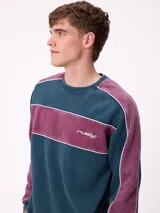 Sweater de cuello redondo marca Rusty, con diseño de bloques de color en azul marino y verde, con detalles de líneas blancas. Presenta el logo de la marca bordado en el pecho.