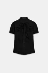 Top de popelín negro de manga corta abullonada, con cuello mao, escote en pico con lazada y cierre frontal con botones.