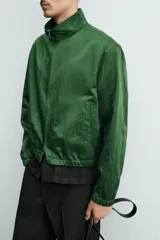Campera verde oscuro de corte cropped y tejido técnico, con cuello alto, cierre frontal de cremallera con tirador circular, bolsillos ribeteados y puños y dobladillo elásticos.