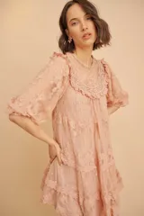 Vestido corto de encaje color durazno, con diseño de volados en capas, mangas largas abullonadas y cuello redondo con detalles bordados.