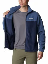 Campera polar Columbia con cierre frontal completo, cuello alto y bolsillos laterales con cierre. Presenta un diseño de bloques de color en dos tonos de azul y el logo de la marca bordado en el pecho.