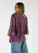 Blusa de algodón color gris oscuro con efecto gastado, mangas largas amplias con múltiples volados escalonados y terminaciones deshilachadas.