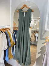 Vestido largo sin mangas, color beige claro, con escote en V y textura arrugada o arrugada, con terminación deshilachada en el ruedo.