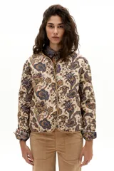 Chaqueta reversible con un lado de twill de lana a cuadros en tonos beige, marrón y gris, con vivos en pana color camel y bolsillos frontales. El otro lado es de algodón capitoneado con estampado de arabescos. Tiene cuello a la base y botones metálicos a presión escondidos.