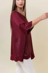 Buzo de tejido liviano con brillo sutil tipo lurex, color beige o dorado claro. Presenta un calce suelto (oversize) con mangas amplias y cuello redondo. El ruedo tiene un detalle de terminación festoneado con pequeños calados.