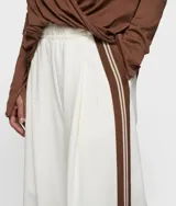 Pantalón ancho de corte oversize, color negro, con cintura alta ajustable con cordón. Presenta pliegues frontales profundos y cintas a rayas color beige/crema en las costuras laterales.