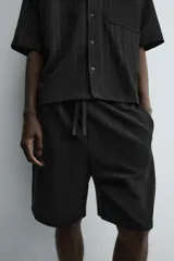 Bermuda de corte relajado color marrón con finas rayas verticales negras. Presenta cintura elástica ajustable con cordón y bolsillos laterales y trasero.