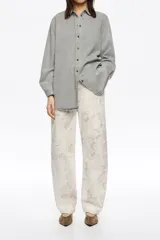 Pantalón de corte barrel y tiro medio, confeccionado en algodón con estampado de textura tipo piel de serpiente en tonos neutros. Presenta diseño de cinco bolsillos, cierre frontal con botón y cremallera, y costuras irregulares en las piernas.