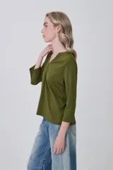 Remera de poliéster color verde oliva, con mangas 3/4, cuello en V con detalle de pliegue central y corte holgado.