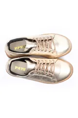 Deportivo de cuero liso color caramelo, con cordones beige y suela blanca. Presenta un detalle metalizado plateado en el talón.