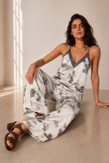 Mono largo de satén con estampado tie-dye en tonos blanco y gris, escote en V con ribete oscuro y tirantes finos ajustables. Presenta un diseño holgado de pierna ancha.