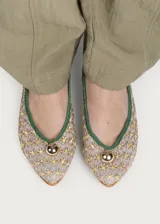 Bailarina de rejilla bordada con diseño de flores pequeñas en tonos beige y amarillo, con ribetes y talón en ante color verde. Presenta un detalle de media esfera metálica dorada en la puntera y suela plana.