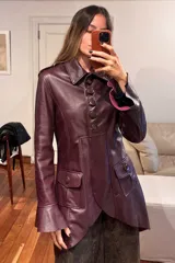 Tapado de cuero ovino color vino, con diseño de corte entallado, mangas largas con volados en los puños y ruedo con volados. Presenta cierre frontal con botones y bolsillos laterales con solapa.
