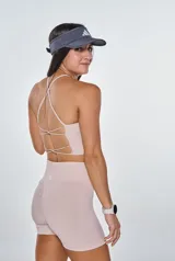 Conjunto deportivo compuesto por un top con espalda de tiras cruzadas y un short de tiro alto con efecto fruncido en la parte trasera. Ambas piezas son de color beige y presentan un diseño ajustado sin costuras.