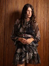 Vestido corto de gasa estampada con diseño abstracto en tonos oscuros, manga larga con volados en los puños y cuello redondo con frunces. Incluye un cinturón de cuero marrón con hebilla metálica.
