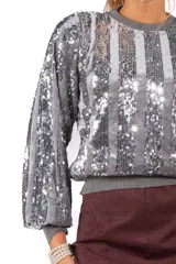 Sweater de cuello redondo y mangas largas abullonadas, confeccionado con un diseño de rayas verticales alternadas entre tejido liso y lentejuelas brillantes.