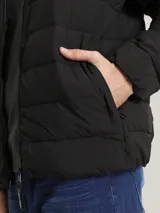 Campera acolchada negra, con cuello alto y cierre frontal de cremallera. Presenta costuras horizontales que crean un efecto acolchado y un parche con el logo de Calvin Klein en la manga izquierda.