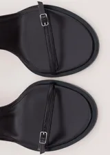 Sandalias de tacón alto color negro, con diseño minimalista de tiras finas cruzadas en el empeine y cierre con hebilla en el tobillo.