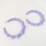 Par de aros tipo argolla de resina color lila, con diseño que imita cañas de bambú.