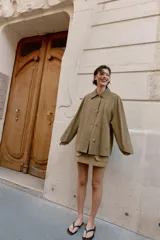 Chaqueta de corte recto y estilo camisero en color beige, con cuello solapa, manga larga y cierre frontal con botones. Presenta dos bolsillos delanteros de plastrón.