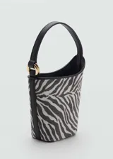 Bolso tipo bucket con estampado cebra, asa corta, cierre de botón magnético, detalle metálico y forro interior.