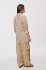 Camisa de rayas de calce relajado, confeccionada en tejido liviano y semitransparente, con cuello clásico, cierre frontal con botones, mangas largas con puños y hombros caídos.