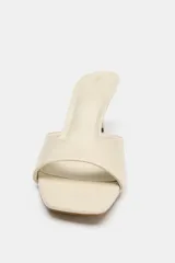 Sandalia de tacón tipo mule color beige, con tira ancha delantera, tacón fino alto y punta redondeada.