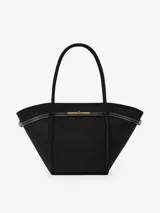 Bolso tipo shopper de eco suede negro con forma trapezoidal, asas de hombro y cierre principal magnético. Presenta detalles en cuero y costuras blancas visibles en el borde superior. Incluye bolsillo interno y correa larga desmontable.