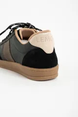 Zapatilla urbana de caña baja, con capellada combinada en tonos verde oscuro, marrón y negro. Presenta puntera y talón en gamuza negra, detalles en cuero marrón en el lateral y forro interior color beige. La suela es de goma color caramelo.