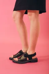 Sandalias de cuero con textura grabada, diseño de punta abierta y talón descubierto con tira ajustable. Poseen una suela de plataforma dentada en tono tierra.