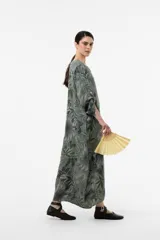Vestido largo de lino de calce relajado y silueta fluida, con estampa botánica en tonos verdes y azules sobre fondo beige. Cuenta con escote en V y mangas amplias.