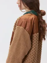 Campera tejida de punto grueso con diseño multicolor. Presenta cuello en contraste de color verde, cuerpo en tono beige con textura trenzada, bolsillos delanteros con apliques en nylon color marrón y bordó, y detalles en nylon en los hombros. Cuenta con cierre frontal de botones y forro interno.