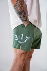 Short deportivo de color verde militar, con diseño estampado en blanco que incluye números y alas. Presenta aberturas laterales en el ruedo para mayor movilidad y bolsillos laterales.