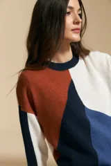 Sweater de tejido de punto con diseño geométrico de bloques de color en tonos tierra, marrón, ocre y blanco. Presenta cuello redondo, mangas largas y un corte relajado.