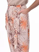 Pantalón babucha de tiro alto con cintura fruncida y lazo para ajustar. Estampado de hojas tropicales en tonos naranja y marrón sobre fondo blanco.
