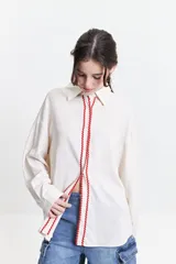 Camisa oversize color crema con detalles de puntilla roja en el frente.
