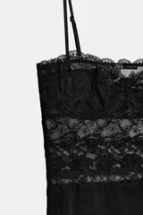Vestido midi negro con escote recto y tirantes finos ajustables. Presenta un cuerpo superior con detalle de encaje floral y copas estructuradas, mientras que la falda es de corte recto y tejido liso.