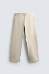 Pantalón chino de algodón color beige claro, corte recto, con cierre frontal de cremallera y botón, bolsillos delanteros y bolsillos traseros de doble vivo con botón.