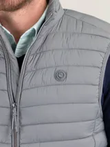 Chaleco acolchado de hombre color gris, con diseño matelasseado horizontal, cuello alto y cierre frontal completo. Presenta un calce ajustado y detalle de logo circular bordado en el pecho.
