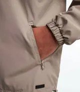 Campera rompevientos color verde oliva con capucha ajustable con cordón, cierre frontal con cremallera, bolsillos laterales con cremallera, puños con elástico y forro interior. Ligera y versátil, ideal para proteger del viento y la lluvia ligera.