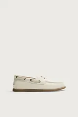 Mocasines tipo náutico de piel en color blanco, con suela plana de goma marrón, cordones y ojalillos metálicos laterales.