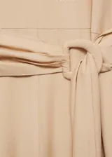 Mono largo de diseño recto, color beige, con cuello redondo, mangas cortas y cierre de botón en la parte posterior. Incluye un cinturón integrado con hebilla del mismo tejido para ajustar a la cintura.