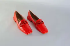Mocasines rojos de cuero con textura tipo cocodrilo y detalle de cadena gruesa en el empeine.