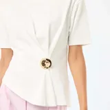 Camiseta blanca de manga corta y cuello redondo, con diseño drapeado en el lateral y detalle de adorno metálico dorado en la cintura.
