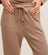 Conjunto de dos piezas color beige, compuesto por un sweater de manga larga con cuello polo y cierre frontal parcial, y un pantalón jogger a juego con cordón ajustable en la cintura.
