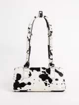 Cartera tipo baguette confeccionada en 100% cuero con estampado animal print tipo vaca en color blanco y negro. Posee doble asa de hombro y broches laterales para ajustar su tamaño.