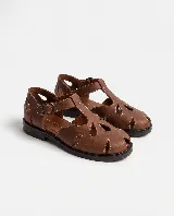 Sandalias de cuero marrón, tipo romanas, con calados orgánicos en la capellada, puntera semi cerrada, tira en T y pulsera regulable con hebilla metálica. Poseen taco bajo y costuras pespunteadas a contratono.