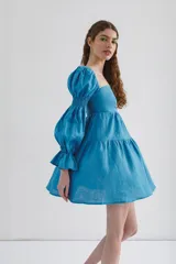 Vestido corto celeste de lino, con escote recto, mangas largas abullonadas con elástico en los puños y falda escalonada.